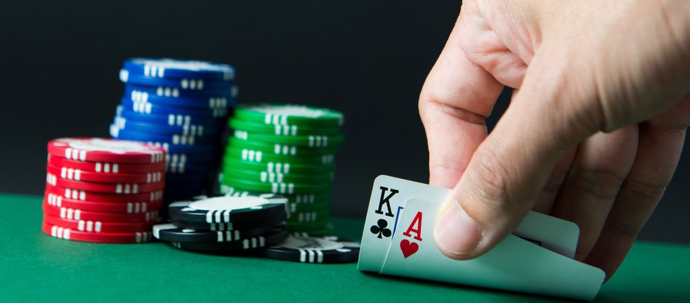 손이 초록색 테이블 위에서 블랙잭 카드를 뒤집고 있으며, 포커 칩 더미가 배경에 놓여 있는 장면